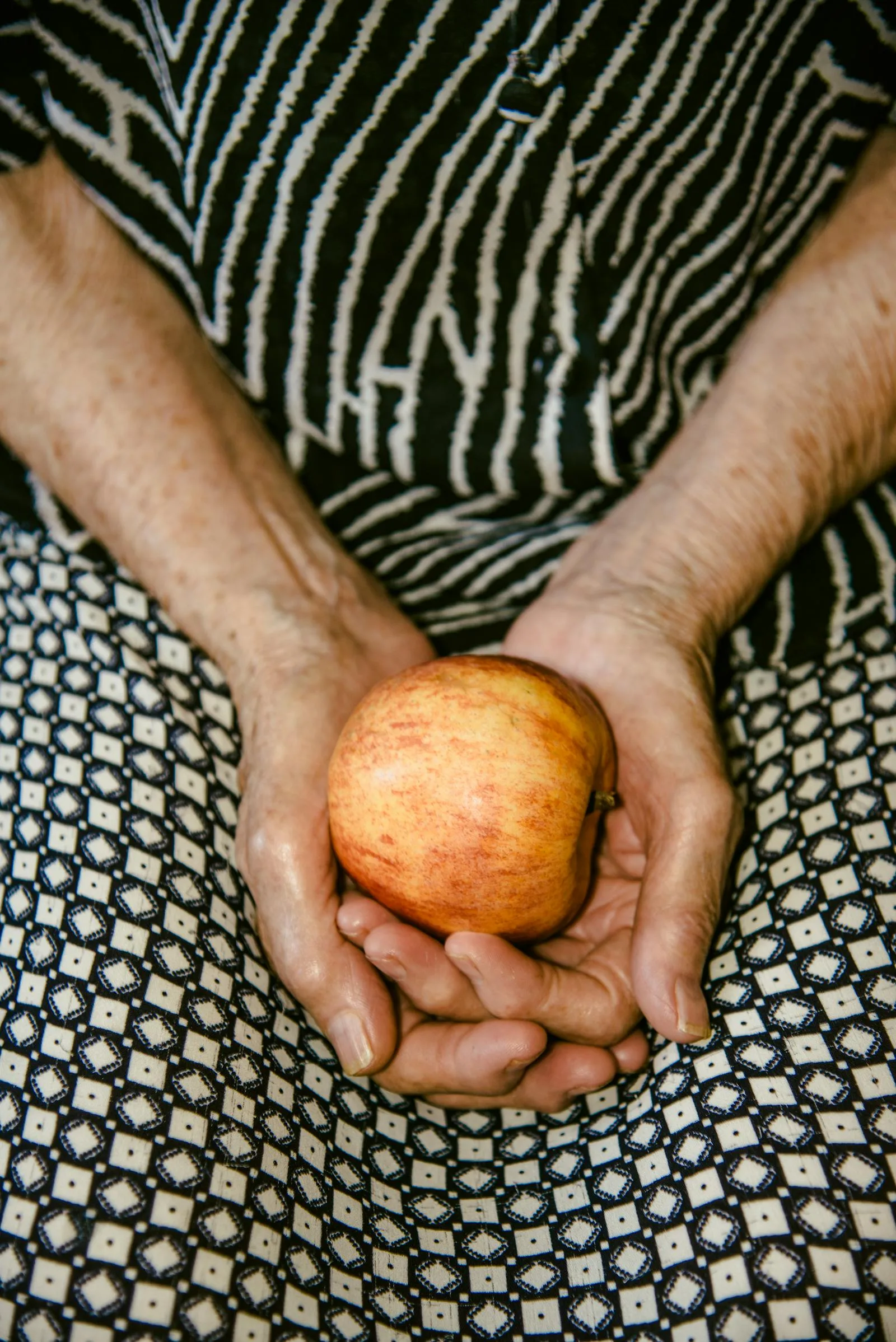 Mains âgées tenant une pomme — symbolique du soin, de la patience et de la transmission